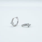 Rhodium-plated sterling silver huggie earrings with clear cubic zirconia floral details on a light background