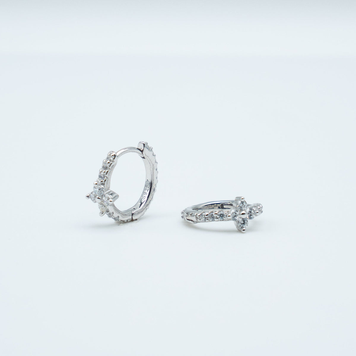 Rhodium-plated sterling silver huggie earrings with clear cubic zirconia floral details on a light background