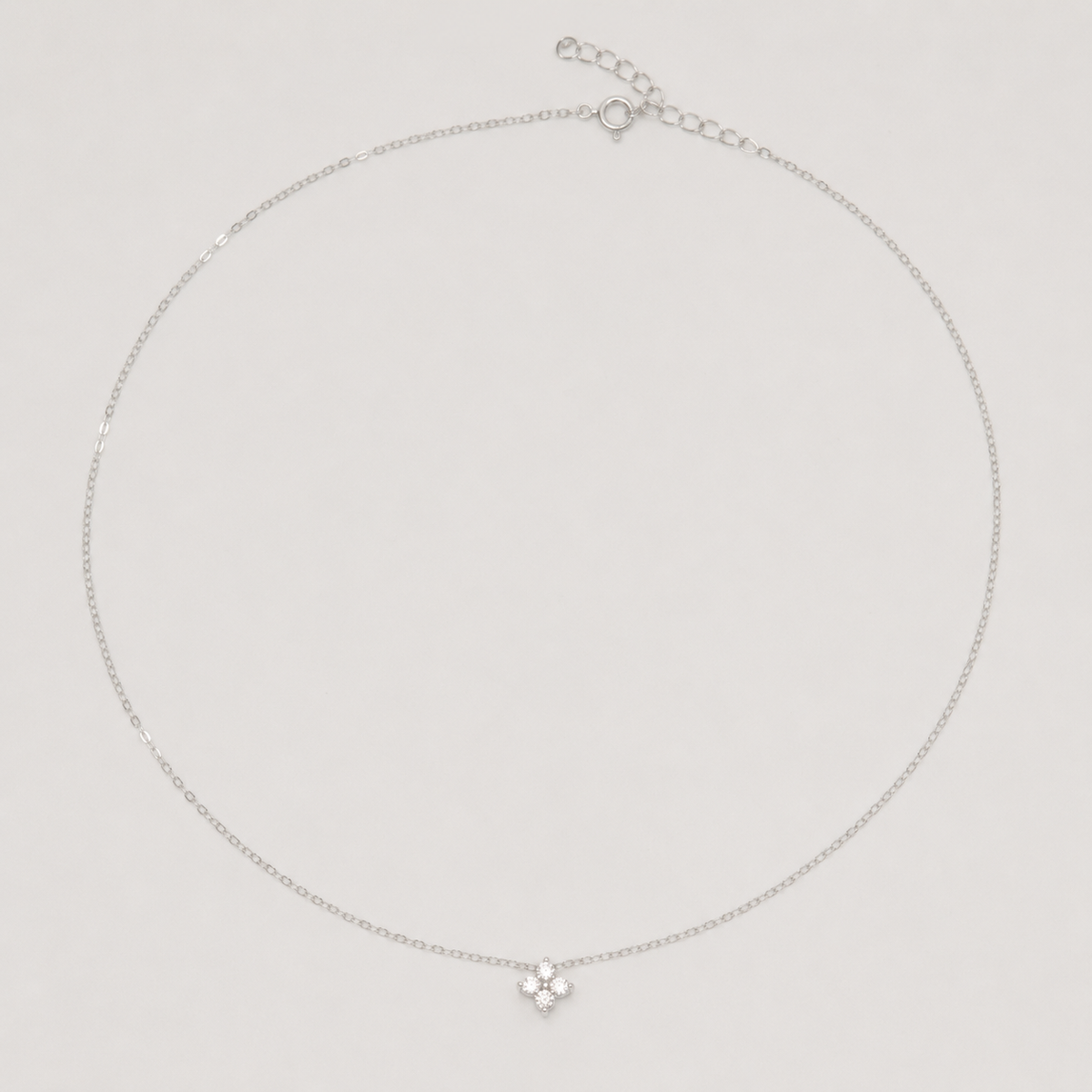 Rhodium-plated sterling silver necklace with a small four-petal cubic zirconia pendant on a light background