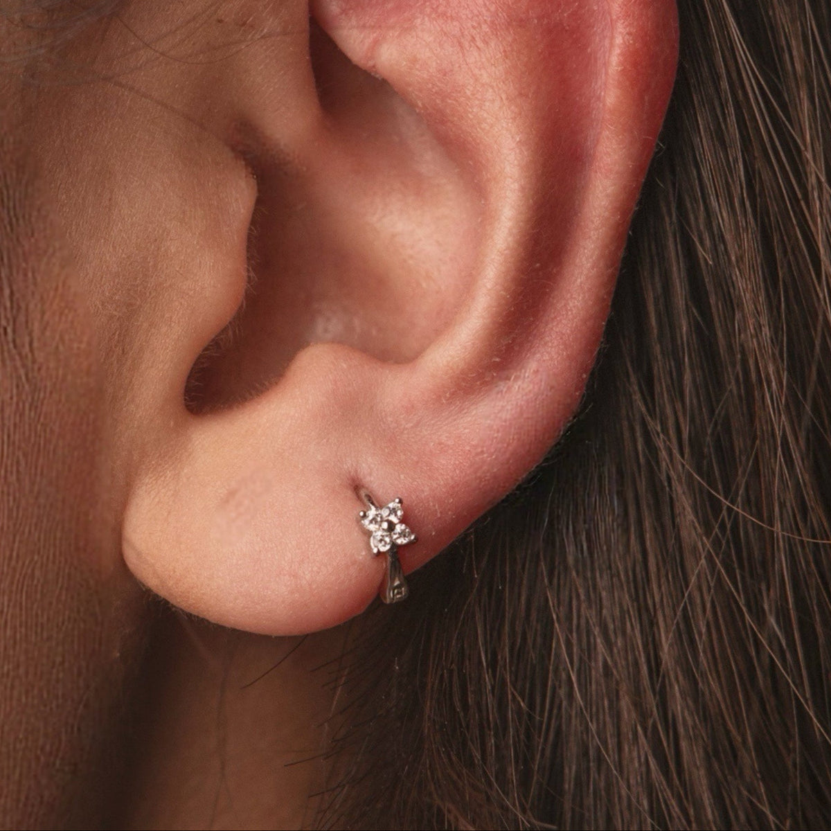 Rhodium-plated sterling silver single earring with a four-petal flower design worn on ear