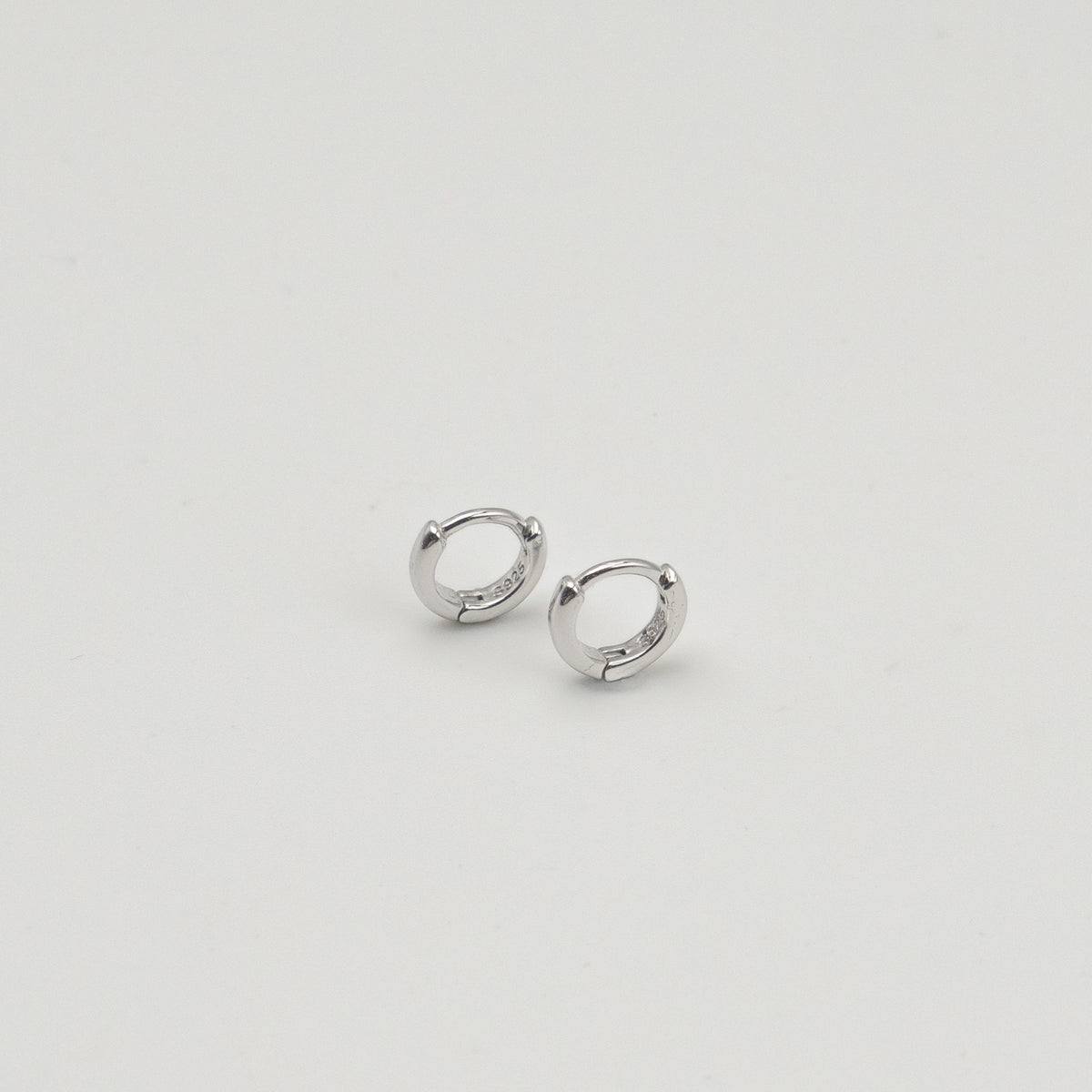 Rhodium-plated sterling silver minimalist huggie earrings with a smooth polished finish on a light background