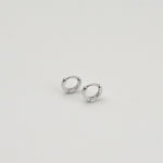 Rhodium-plated sterling silver minimalist huggie earrings with a smooth polished finish on a light background