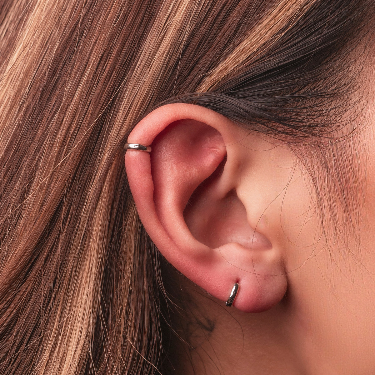 Rhodium-plated sterling silver minimalist huggie earrings with a smooth polished finish worn on ear