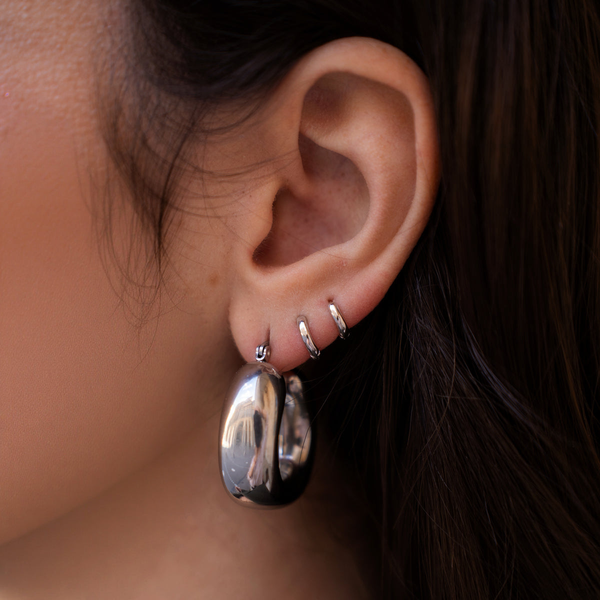 Rhodium-plated sterling silver minimalist huggie earrings with a smooth polished finish worn on ear
