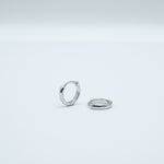 Rhodium-plated sterling silver minimalist huggie earrings with a smooth polished finish on a light background