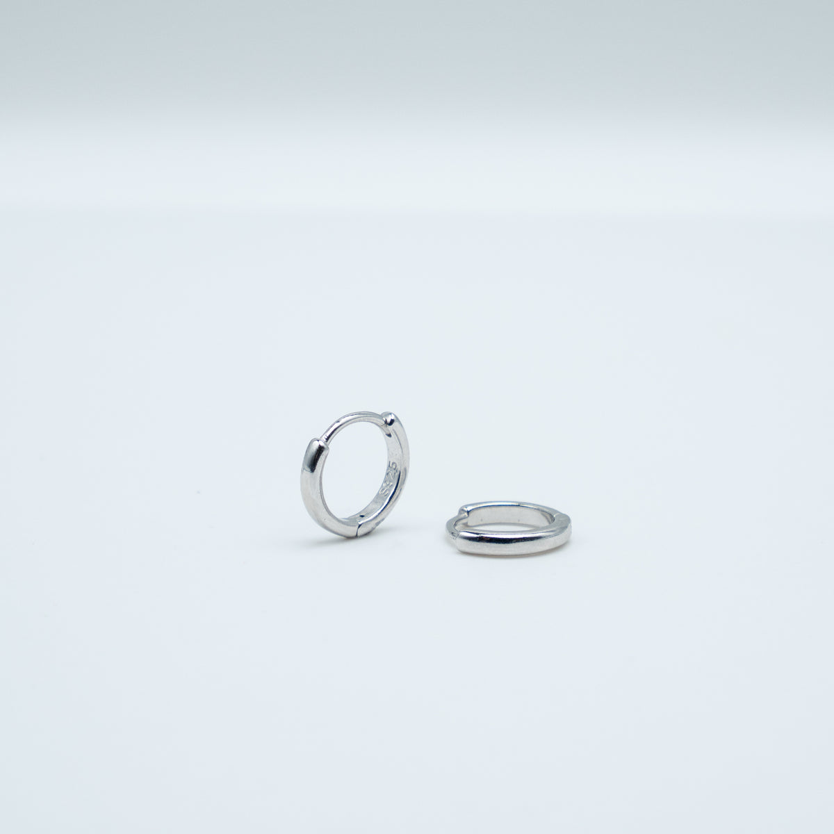 Rhodium-plated sterling silver minimalist huggie earrings with a smooth polished finish on a light background