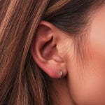 Rhodium-plated sterling silver minimalist huggie earrings with a smooth polished finish on a light background worn on ear