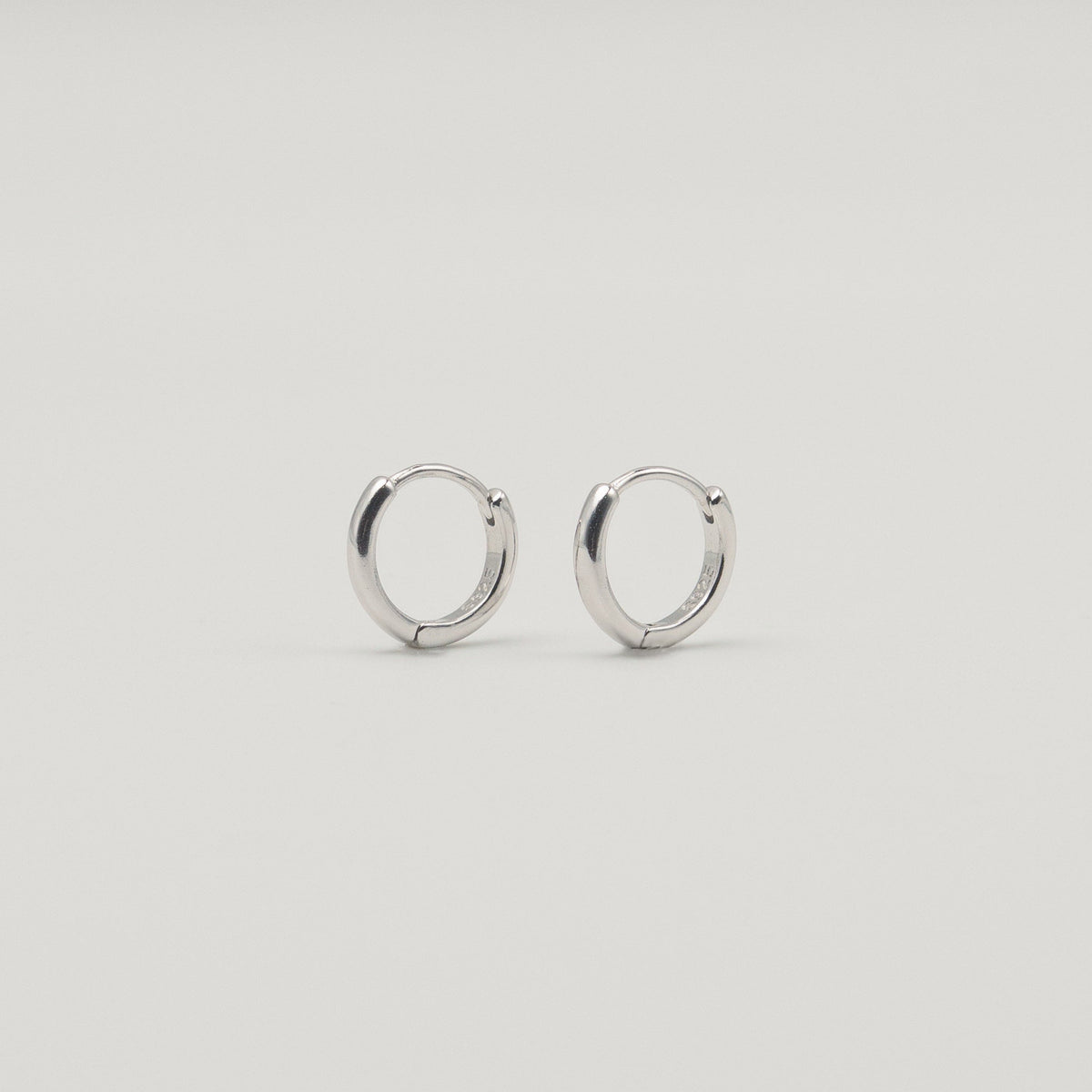 Rhodium-plated sterling silver minimalist huggie earrings with a smooth polished finish on a light background