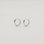 Rhodium-plated sterling silver minimalist huggie earrings with a smooth polished finish on a light background