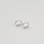 Rhodium-plated sterling silver minimalist huggie earrings with a smooth polished finish on a light background
