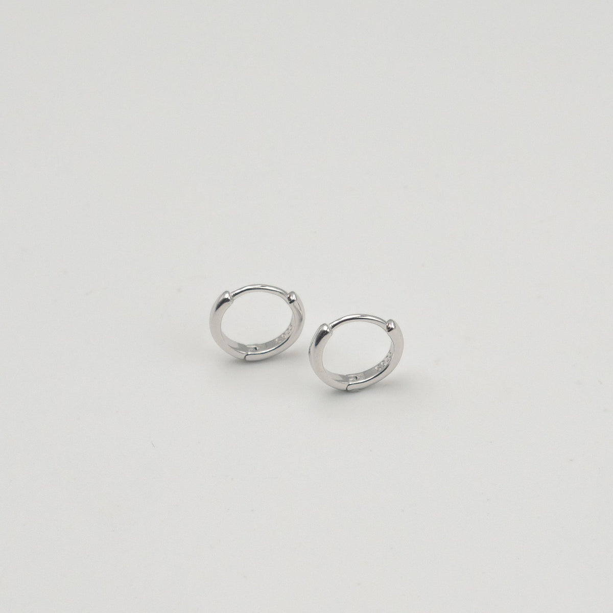Rhodium-plated sterling silver minimalist huggie earrings with a smooth polished finish on a light background
