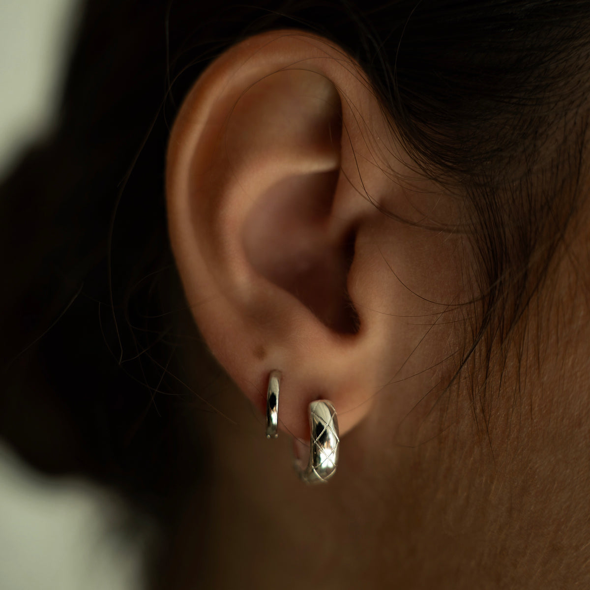 Rhodium-plated sterling silver minimalist huggie earrings with a smooth polished finish worn on ear