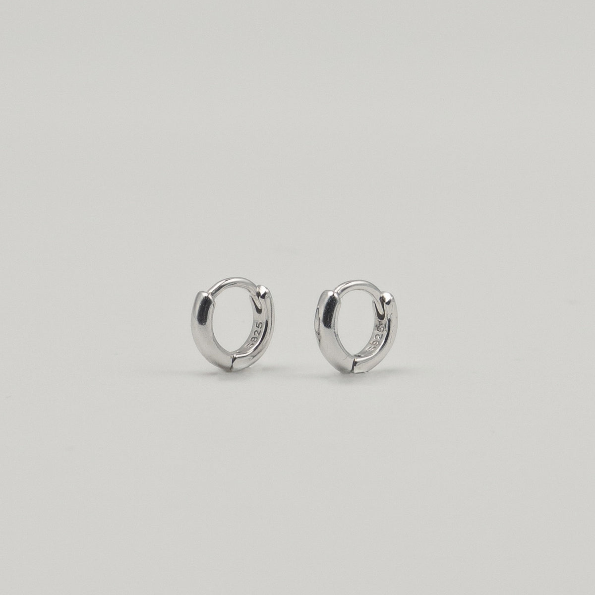 Rhodium-plated sterling silver minimalist huggie earrings with a smooth polished finish on a light background