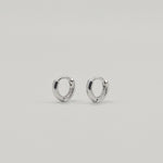 Rhodium-plated sterling silver minimalist huggie earrings with a smooth polished finish on a light background