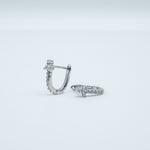 Rhodium-plated sterling silver huggie earrings with pavé cubic zirconia and small clustered stone details on a light background