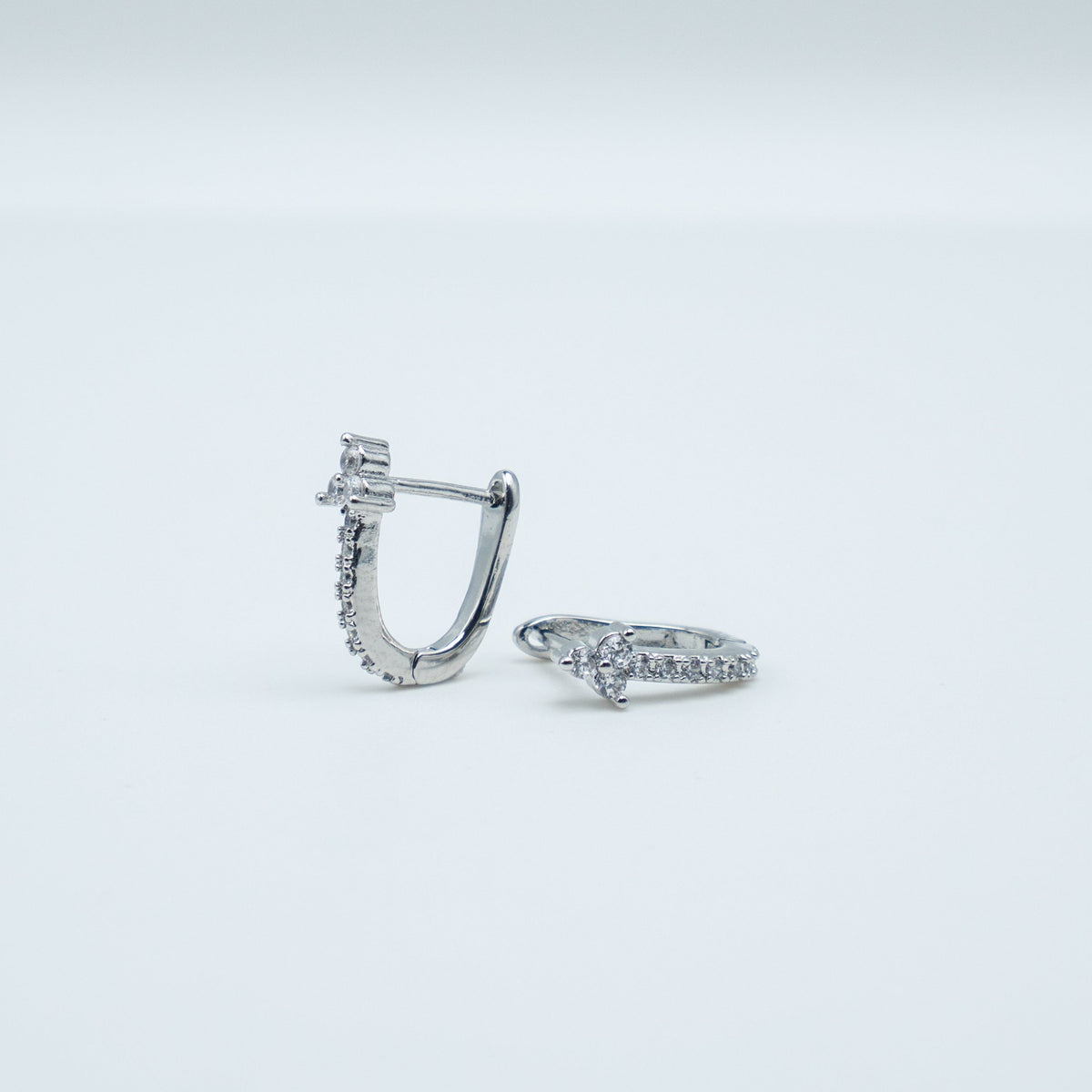 Rhodium-plated sterling silver huggie earrings with pavé cubic zirconia and small clustered stone details on a light background