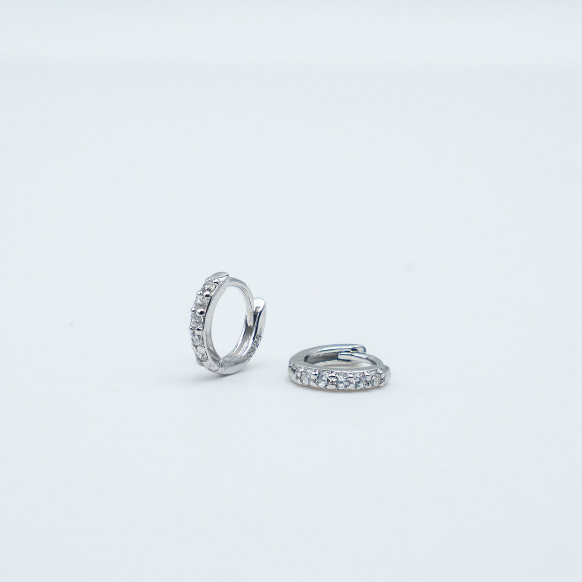 Rhodium-plated sterling silver huggie earrings with clear cubic zirconia pavé stones on a light background