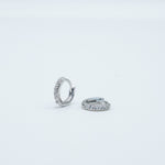Rhodium-plated sterling silver huggie earrings with clear cubic zirconia pavé stones on a light background