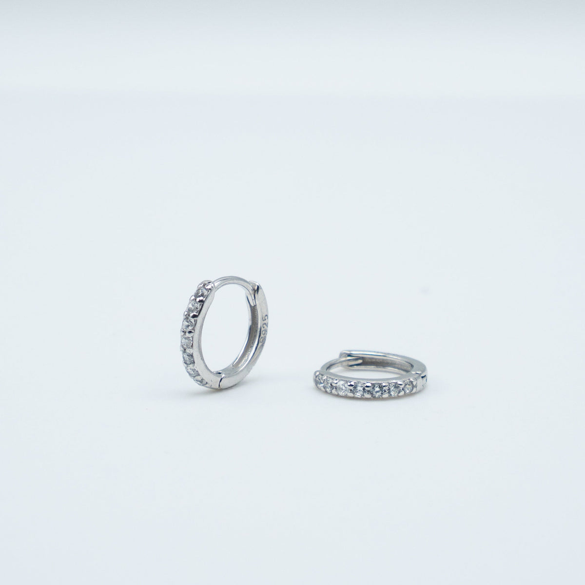 Rhodium-plated sterling silver huggie earrings with clear cubic zirconia pavé stones on a light background
