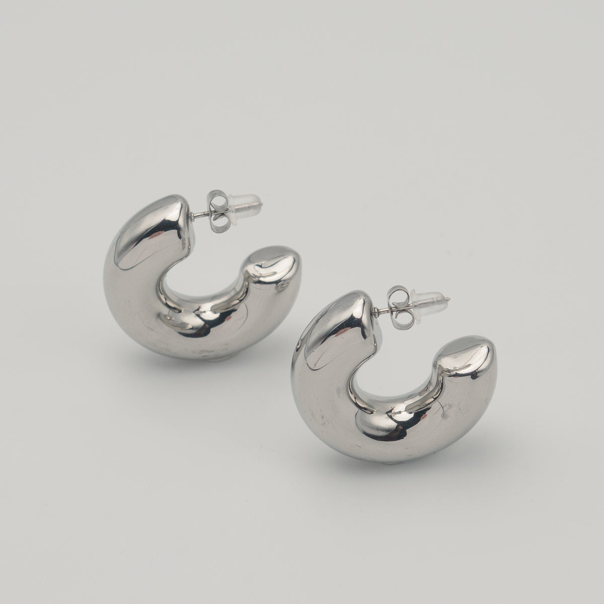 Polished silver stainless steel chunky hoop earrings on a light background