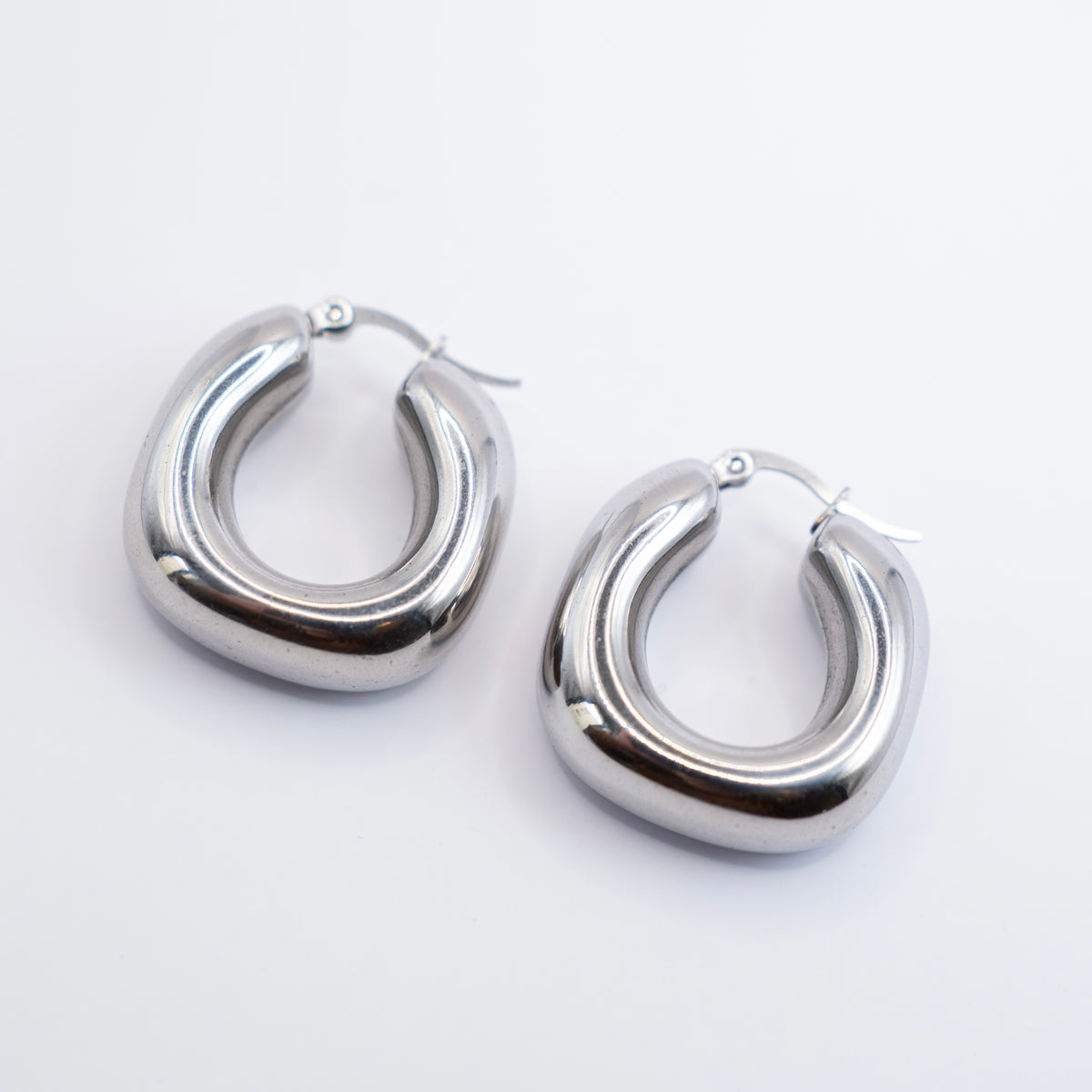 olished silver stainless steel chunky rounded hoop earrings on a white background