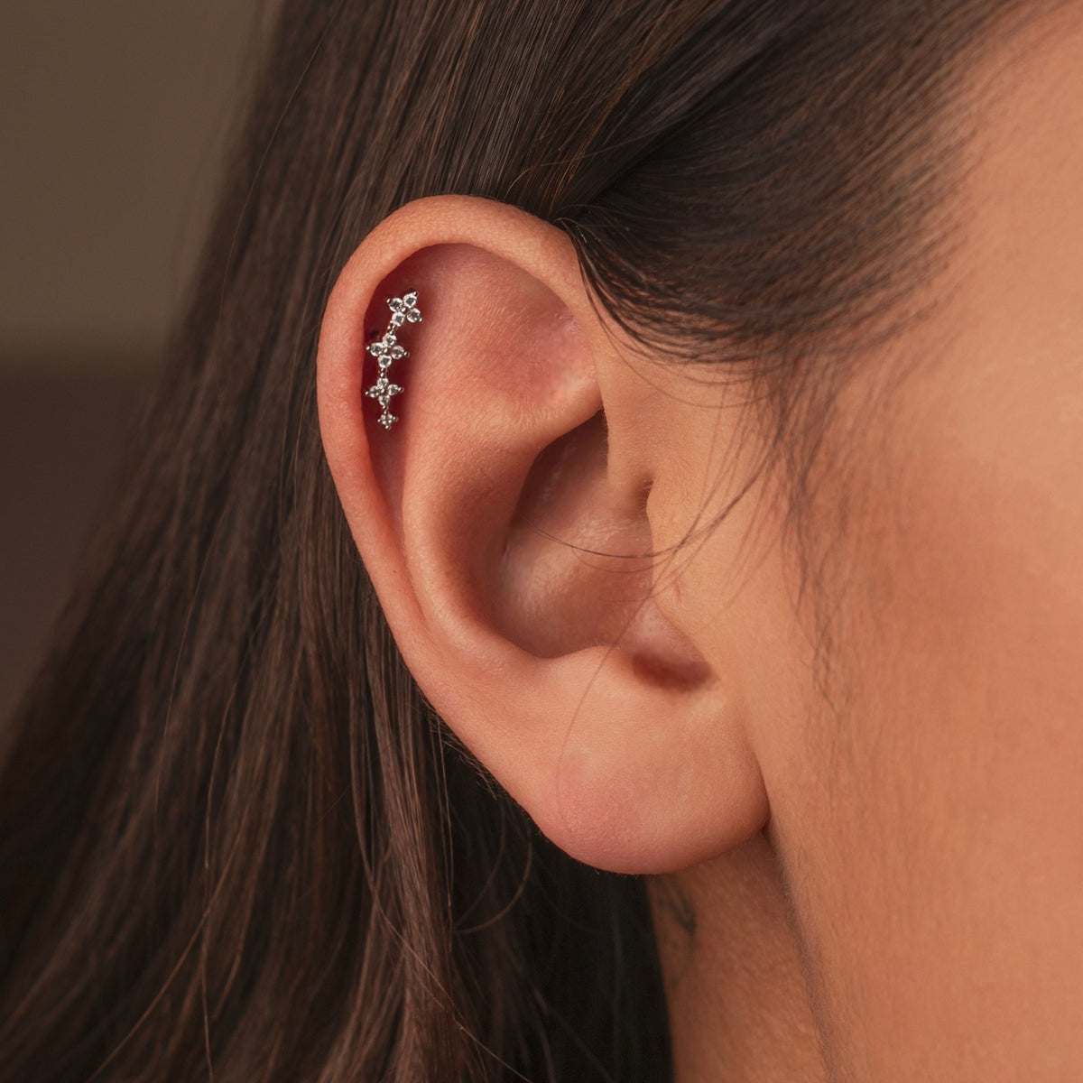 Silver stainless steel clover cartilage earring with cubic zirconia details and round back worn on the ear