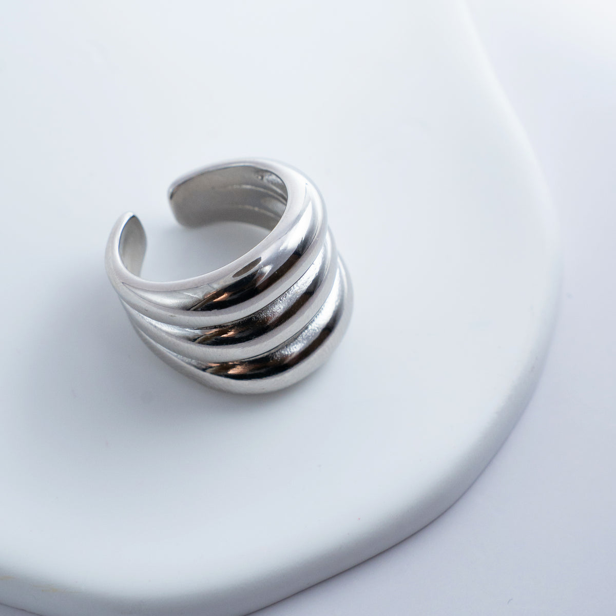 Polished silver stainless steel open ring with a chunky triple-band design on a light background