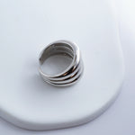 Polished silver stainless steel open ring with a chunky triple-band design on a light background