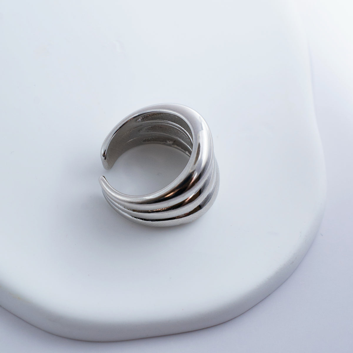 Polished silver stainless steel open ring with a chunky triple-band design on a light background