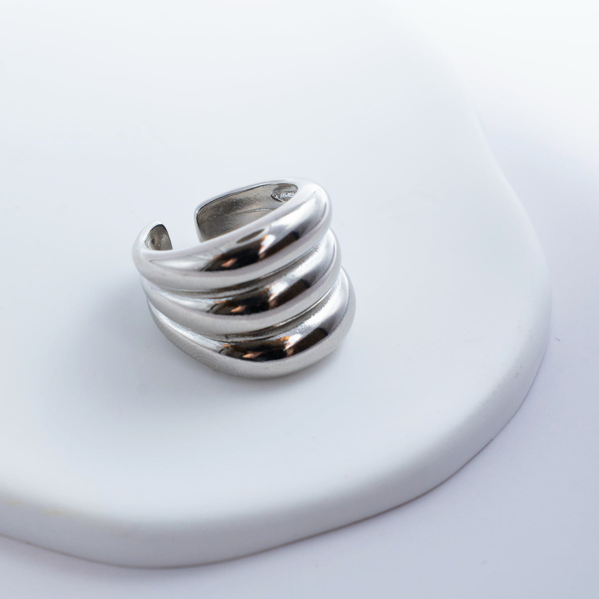 Polished silver stainless steel open ring with a chunky triple-band design on a light background