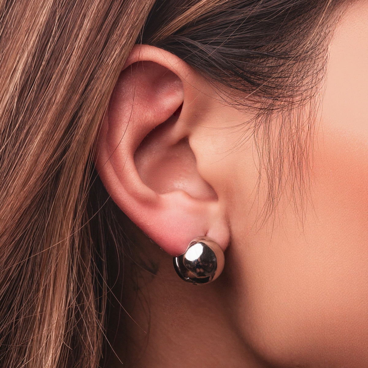 Polished sterling silver chunky clip earrings with a rounded dome shape on a light background worn on the ear